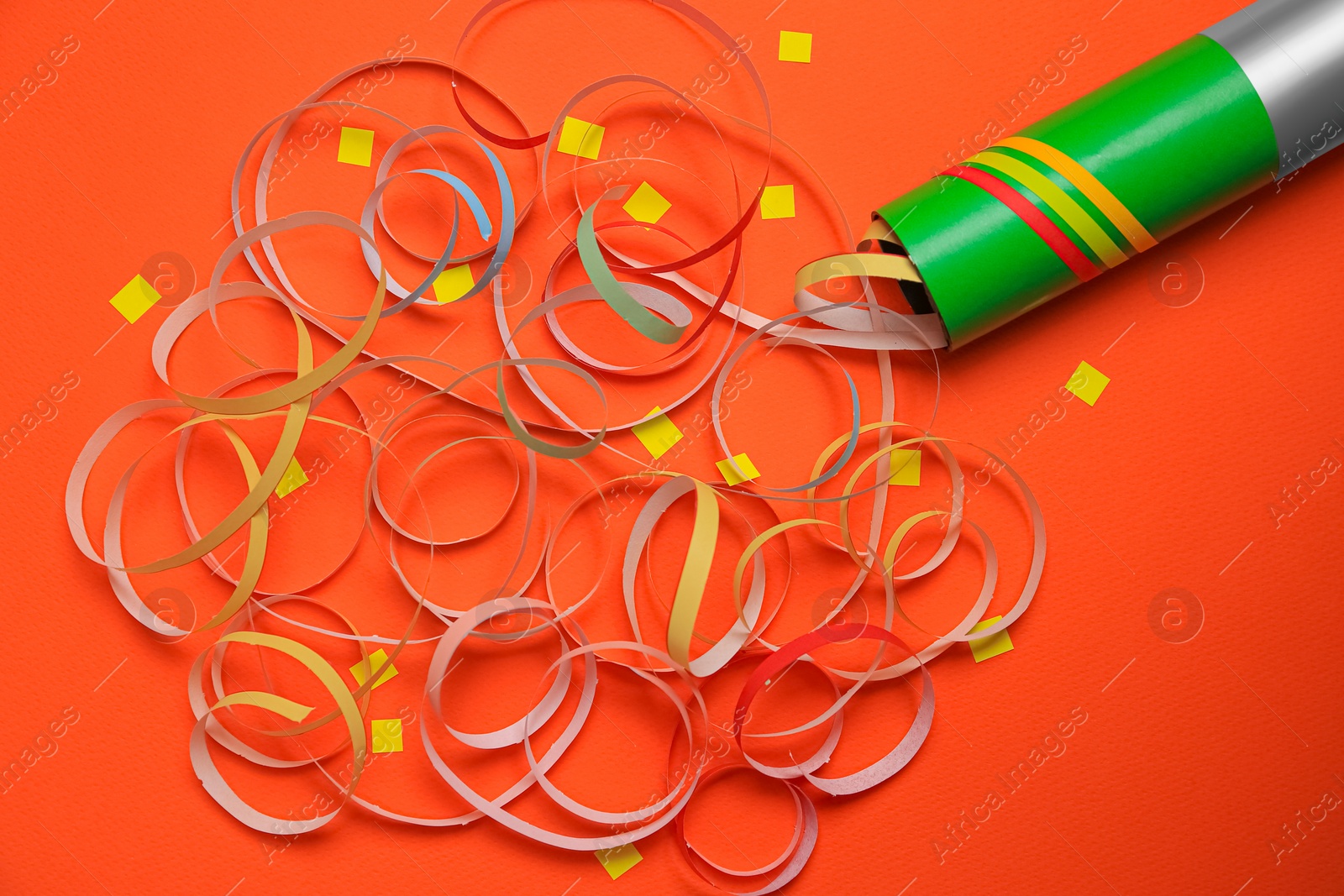 Photo of Beautiful serpentine and confetti bursting out of party popper on orange background, flat lay