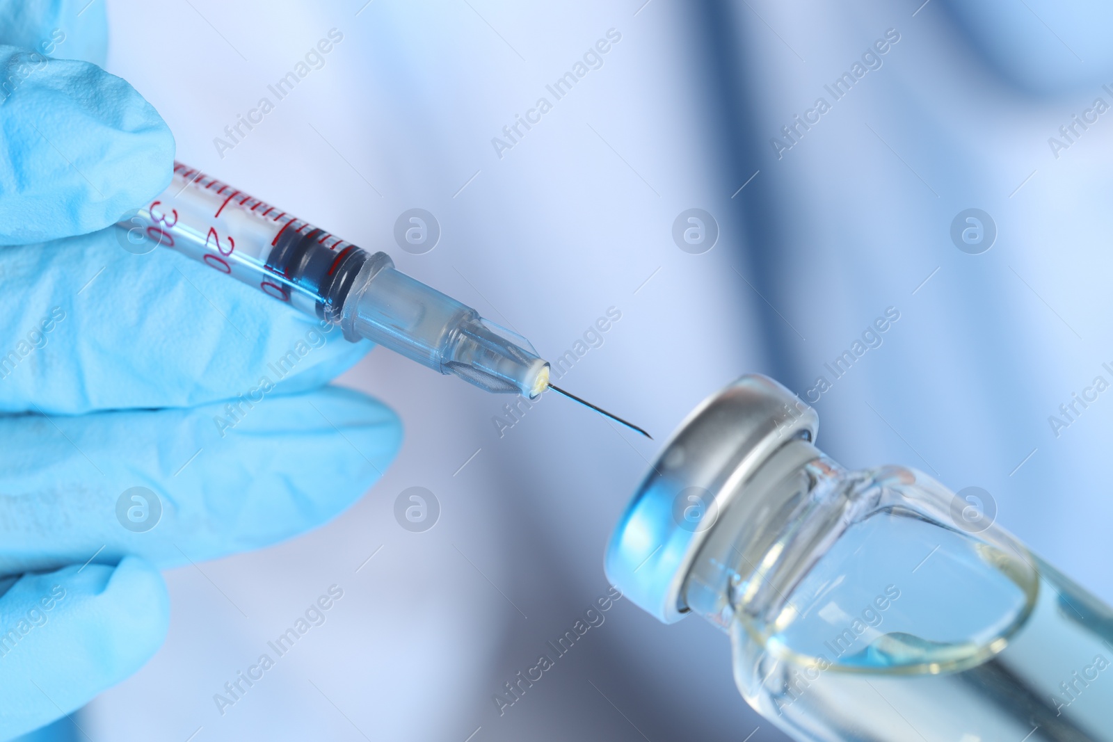 Photo of Doctor inserting syringe into glass vial with medication, closeup