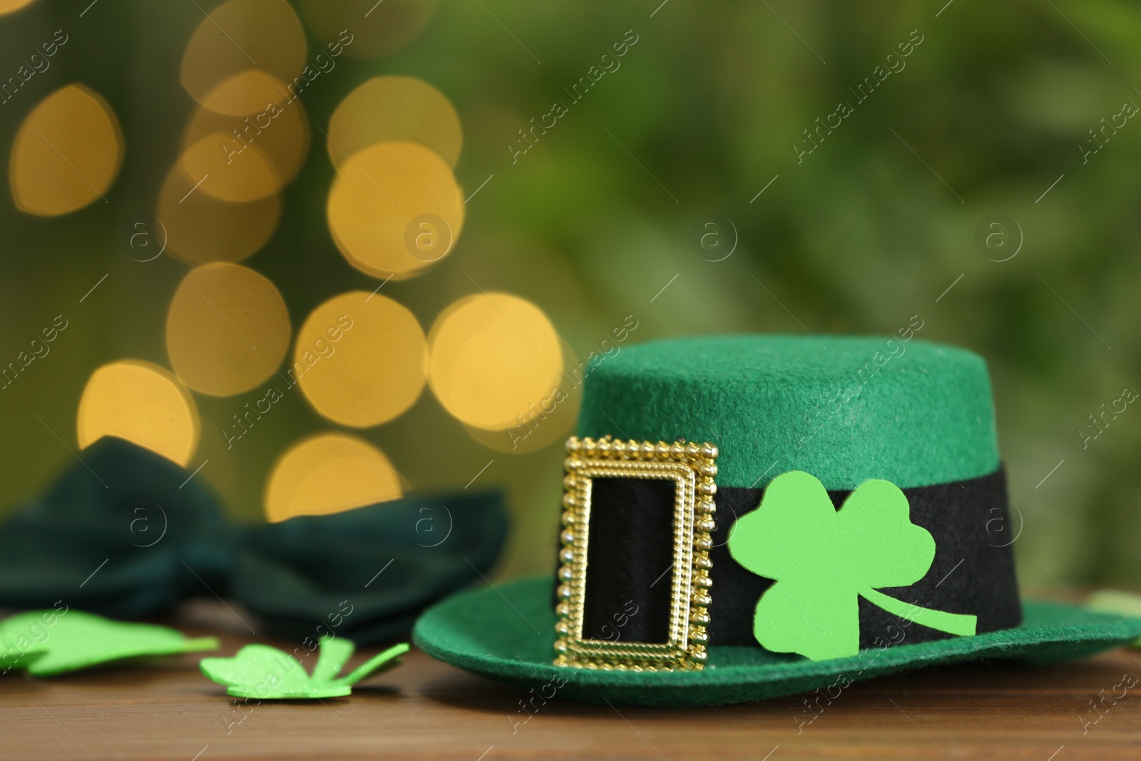 Photo of Leprechaun hat and clover leaves on wooden table against blurred lights, space for text. St Patrick's Day celebration