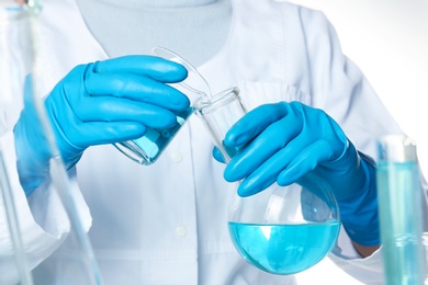 Scientist pouring color liquid from beaker into Florence flask, closeup. Solution chemistry