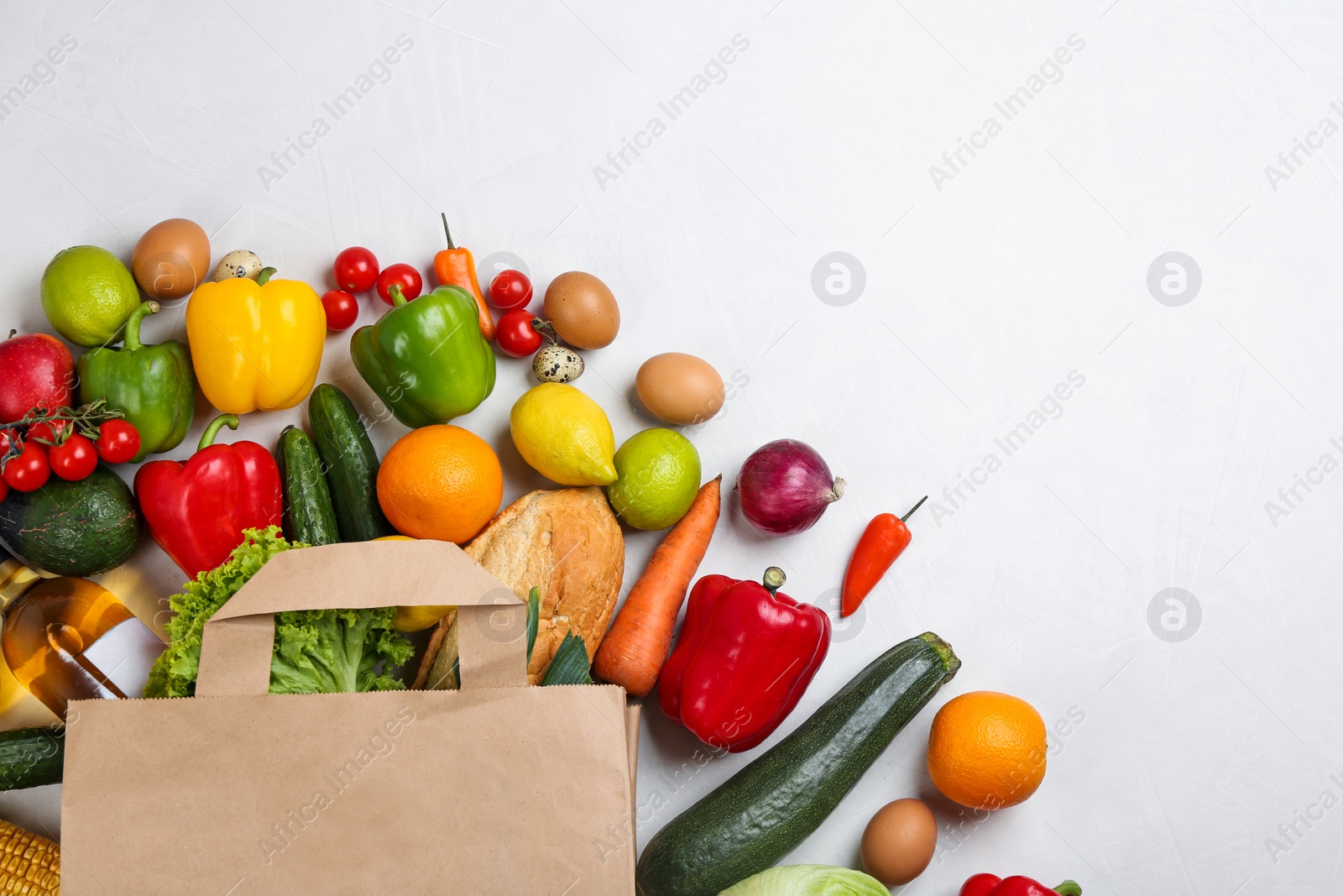 Photo of Flat lay composition with overturned paper bag and groceries on white table. Space for text