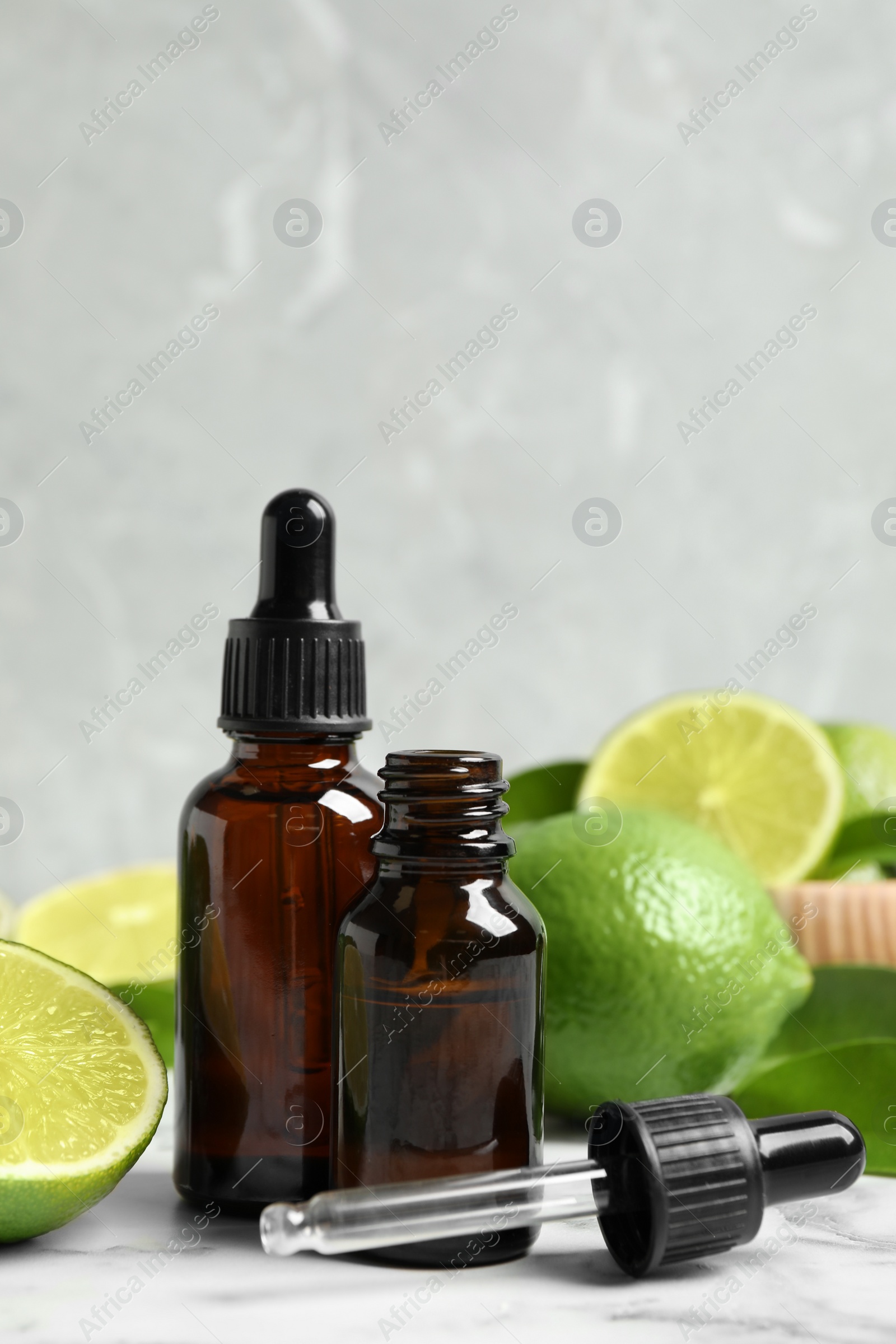 Photo of Lime essential oil and citrus fruits on marble table