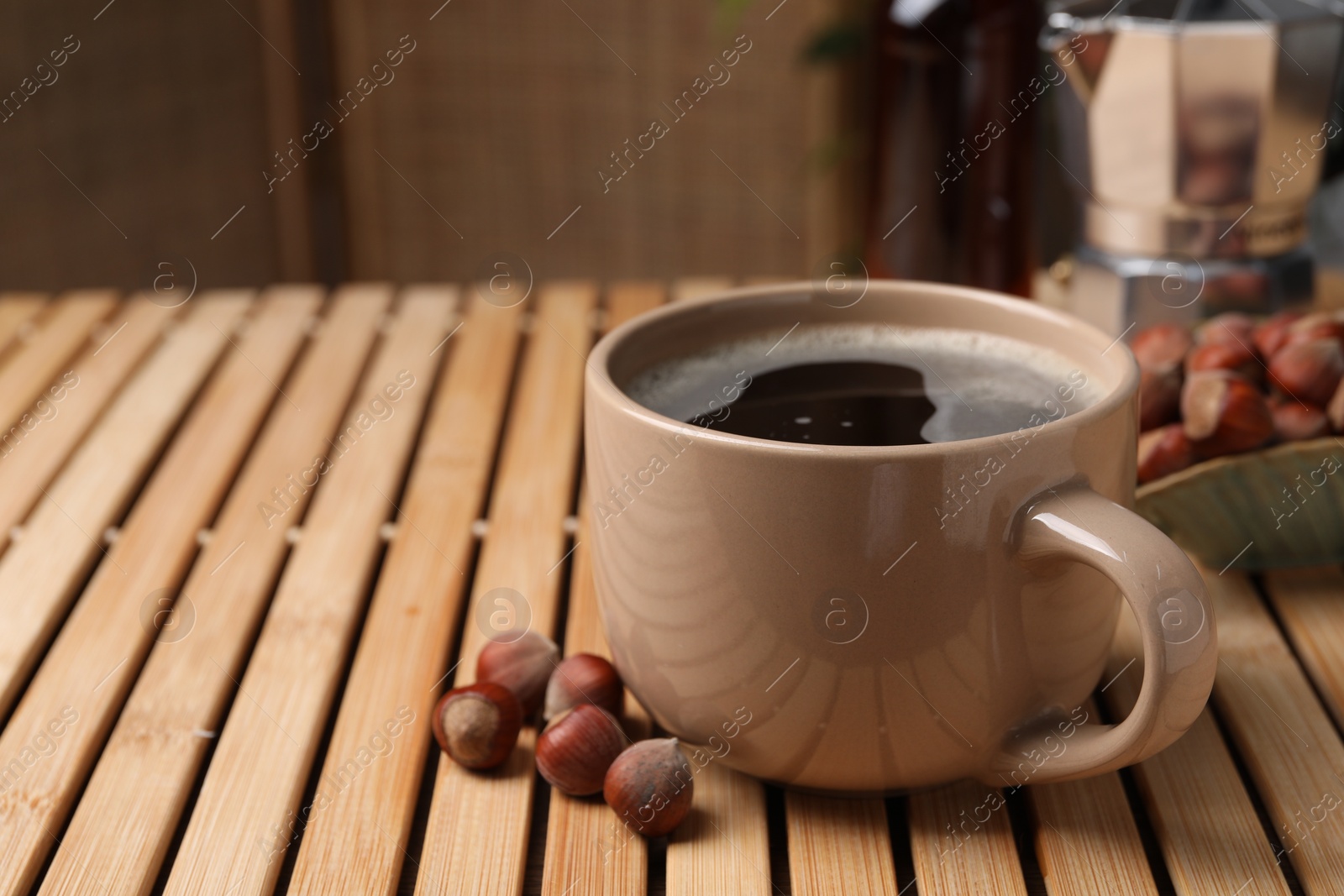Photo of Mug of aromatic coffee with hazelnut syrup on wooden table, closeup. Space for text