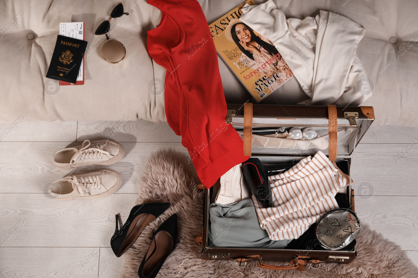 Photo of Open suitcase with clothes, accessories and shoes in living room, top view