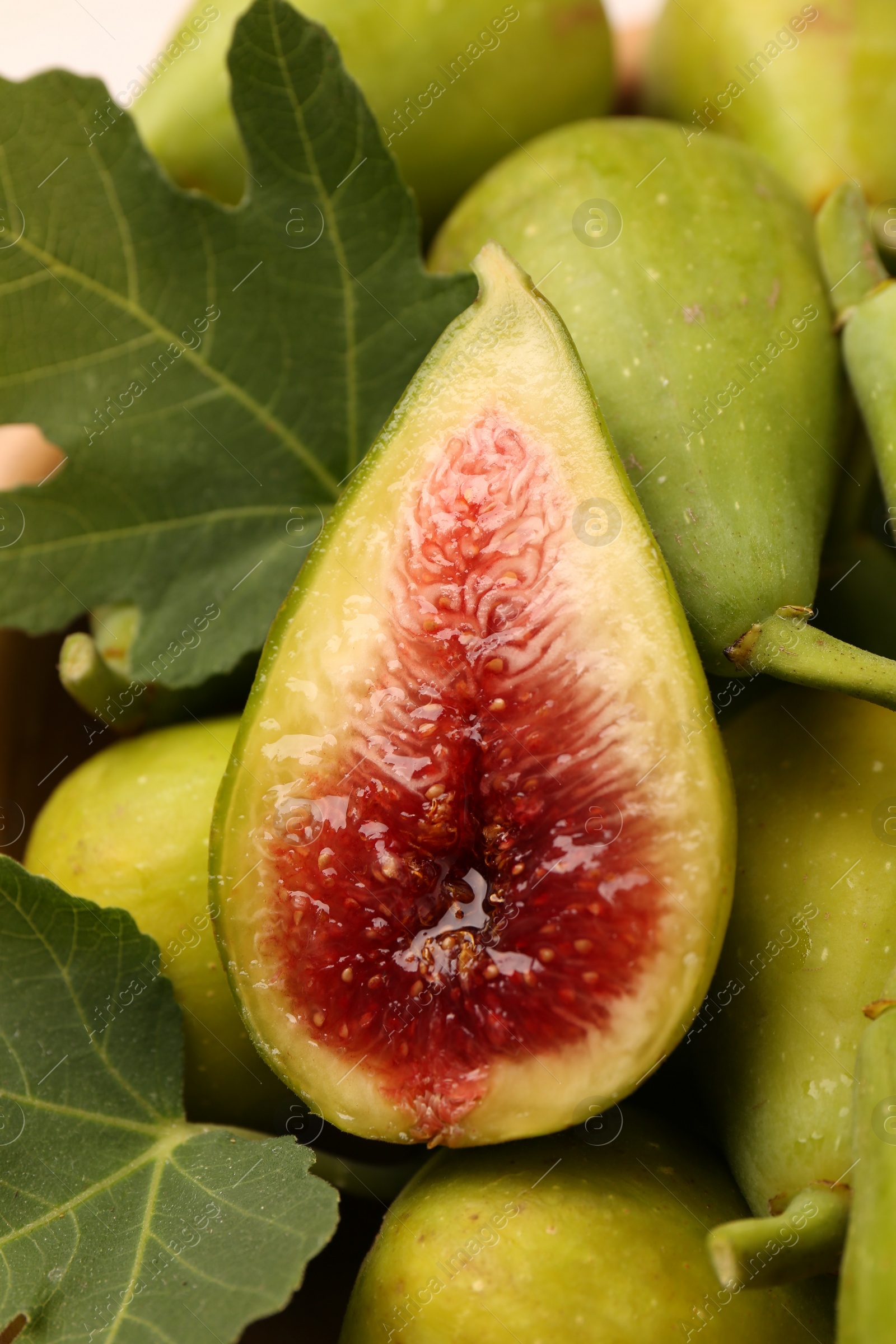 Photo of Cut and whole fresh green figs with leaves as background, closeup