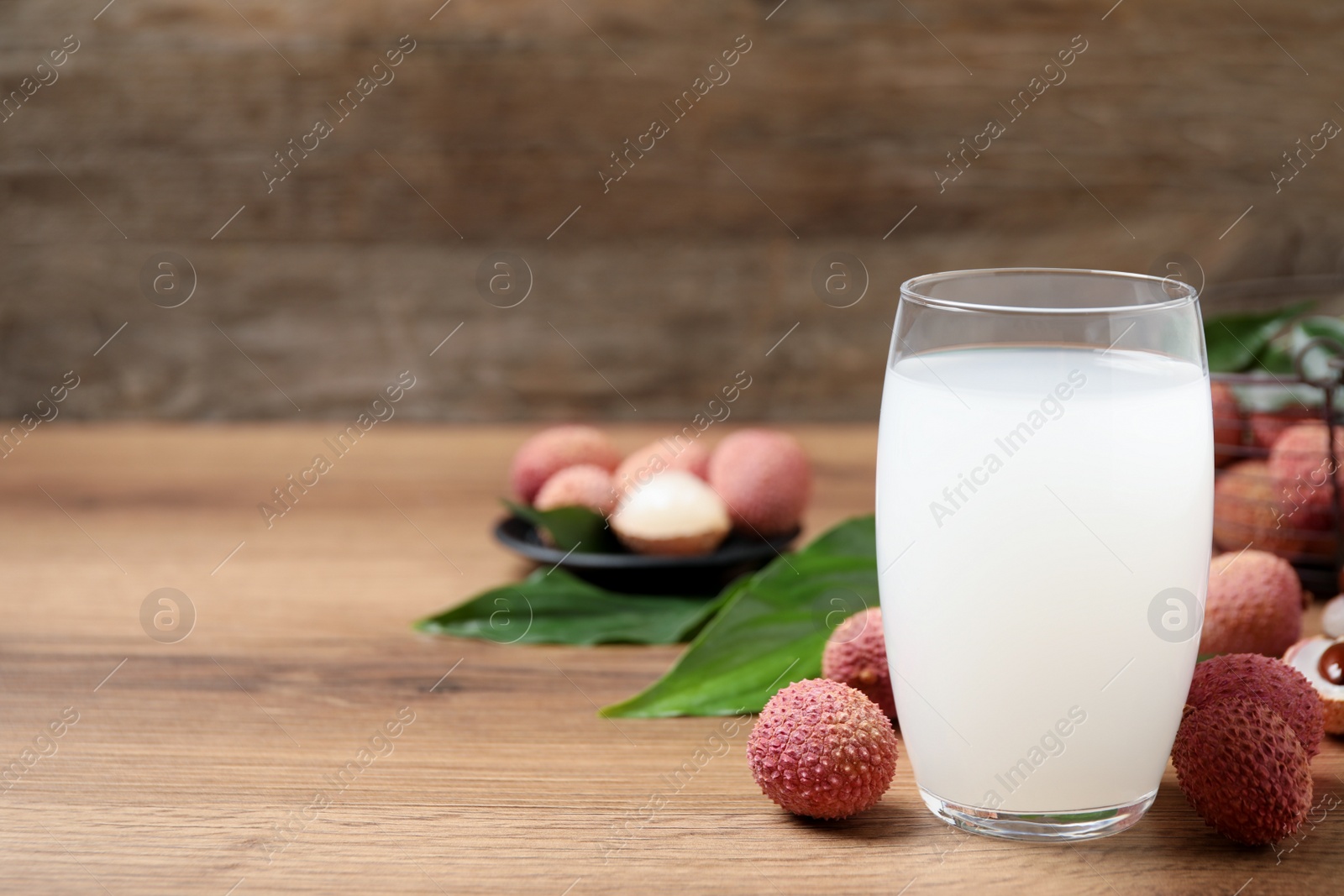 Photo of Lychee juice and fresh fruits on wooden table. Space for text