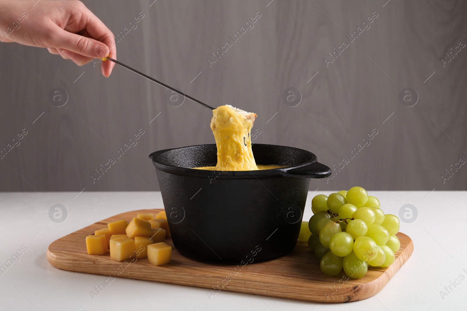 Photo of Woman dipping piece of bread into fondue pot with tasty melted cheese at white table, closeup