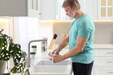 Photo of Senior man washing bowl above sink in kitchen
