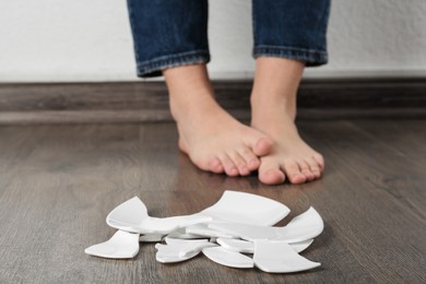 Photo of Barefoot woman standing near broken plate on floor, closeup