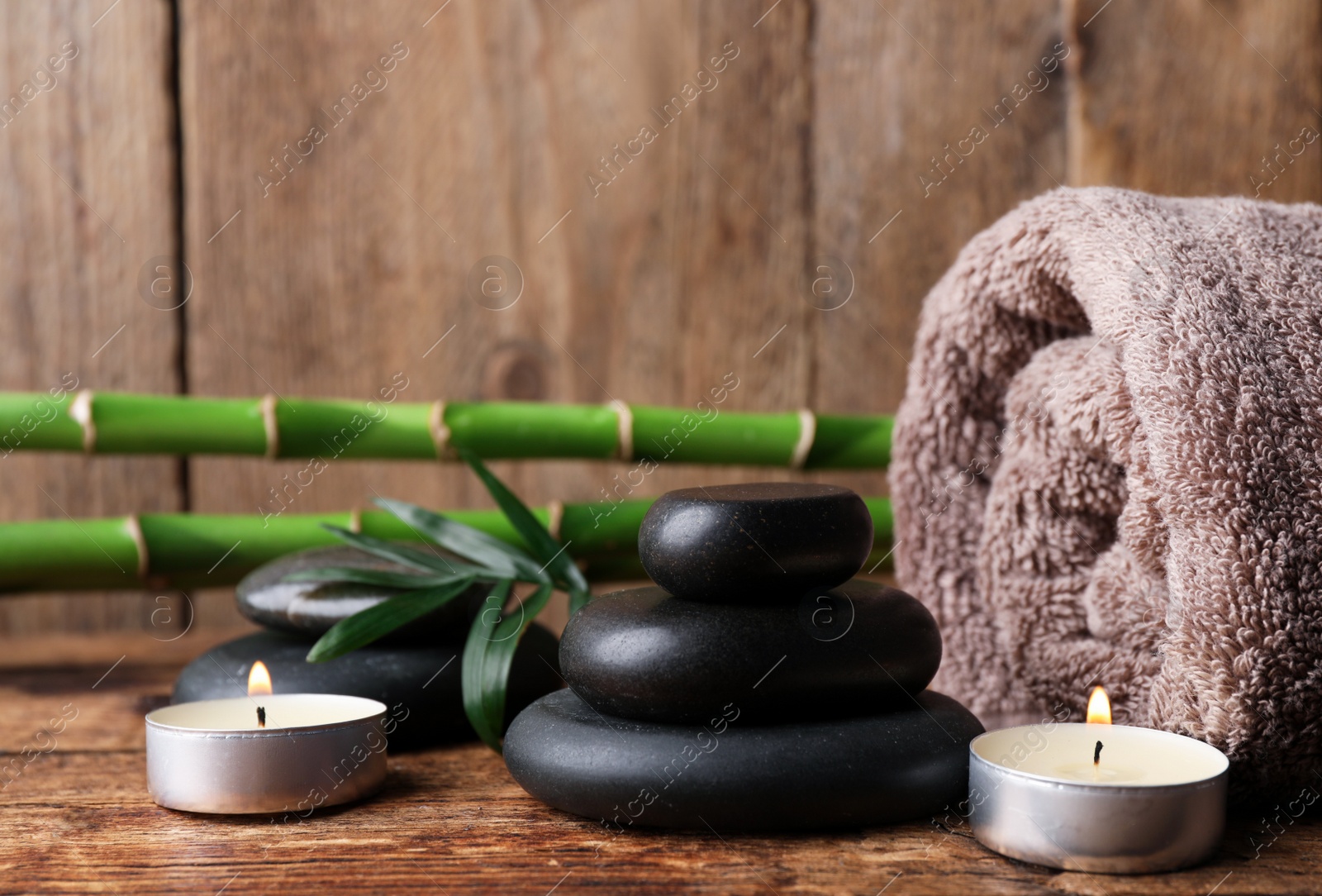 Photo of Stacked spa stones, bamboo, candles and towel on wooden table. Space for text
