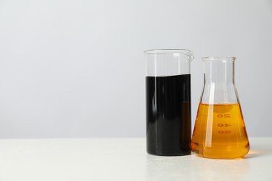 Beaker and flask with different types of oil on white table, space for text