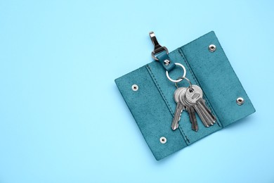 Photo of Leather holder with keys on light blue background, top view. Space for text