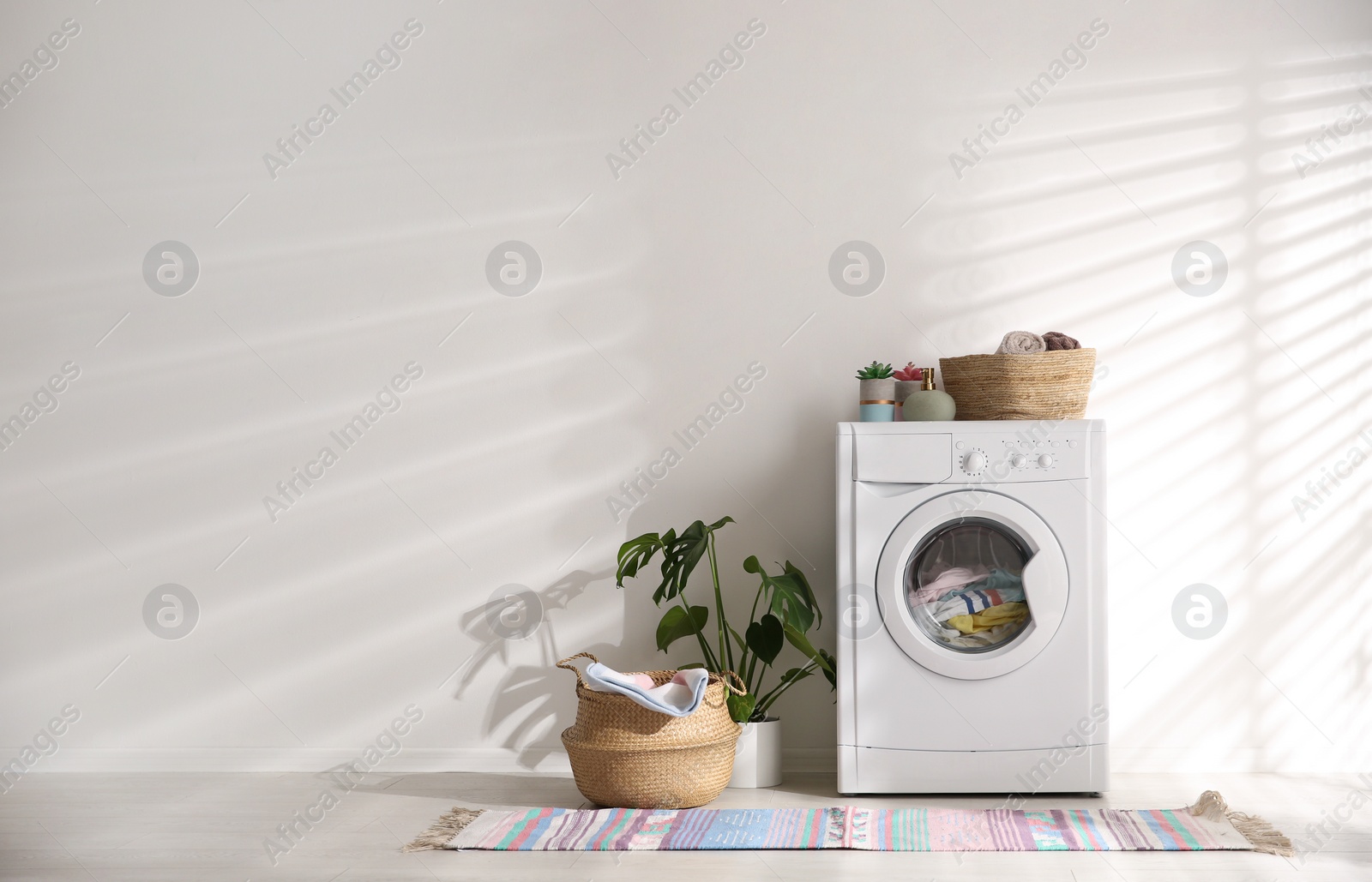Photo of Modern washing machine and wicker basket with laundry near white wall, space for text. Interior design