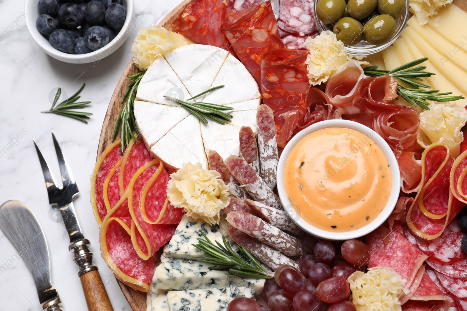 Photo of Wooden plate with different delicious snacks on white marble table, flat lay