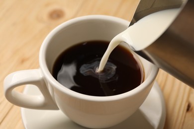 Photo of Pouring milk into cup with coffee at light wooden table, closeup