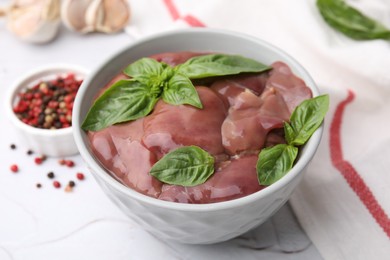 Photo of Bowl with raw chicken liver and basil on white textured table, closeup