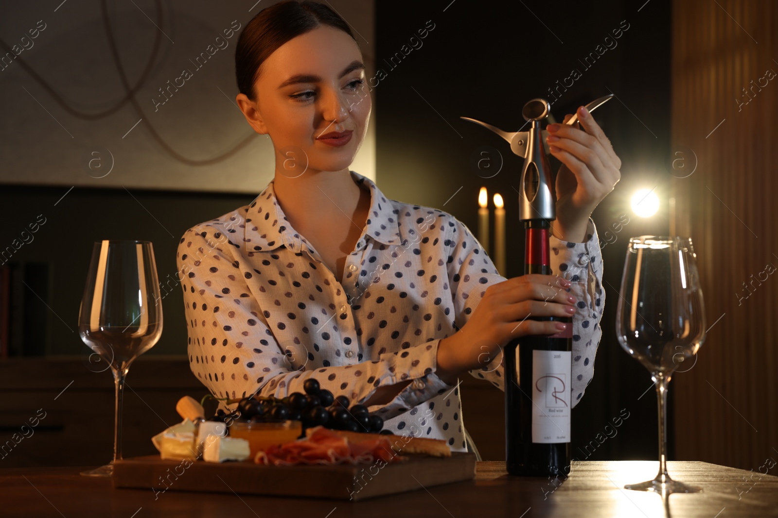 Photo of Romantic dinner. Woman opening wine bottle with corkscrew at table indoors