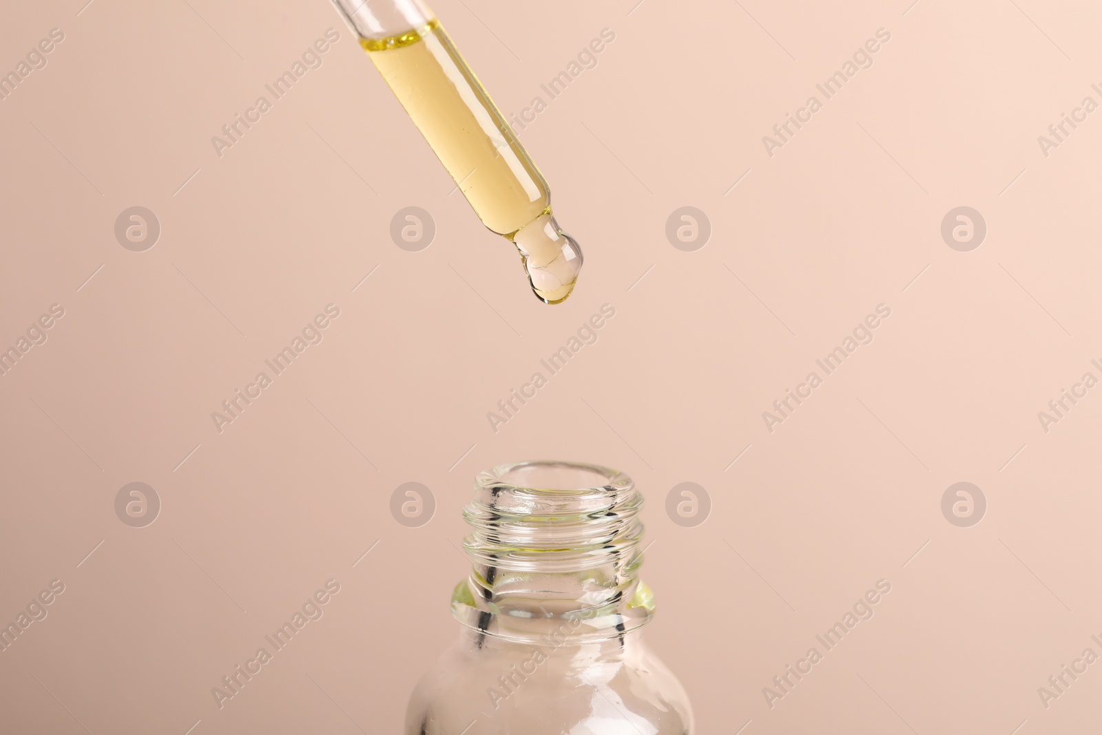 Photo of Dripping cosmetic serum from pipette into bottle on beige background