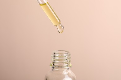 Dripping cosmetic serum from pipette into bottle on beige background