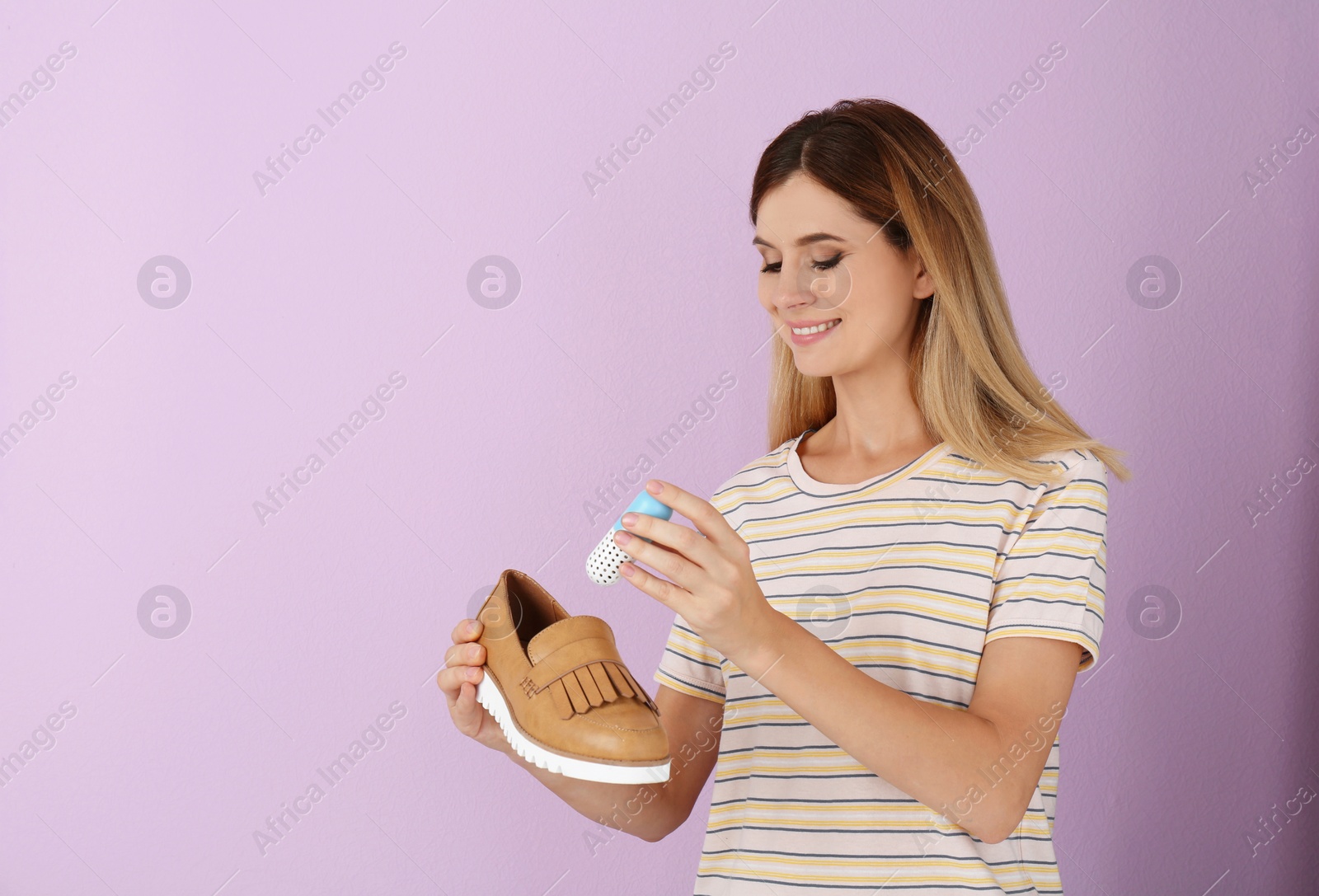 Photo of Woman putting capsule shoe freshener in footwear on color background