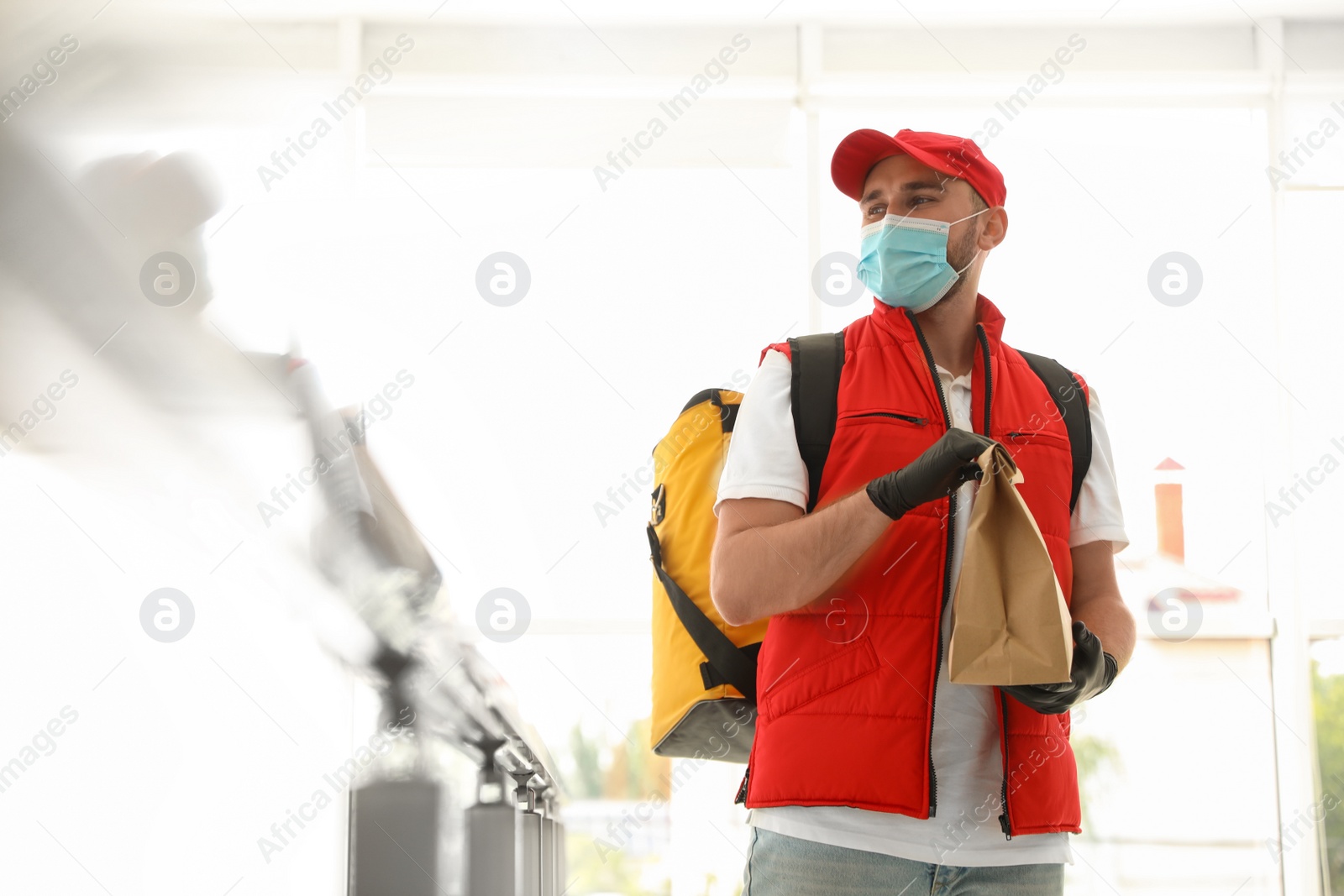 Photo of Courier in protective mask and gloves with order indoors. Restaurant delivery service during coronavirus quarantine