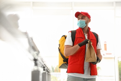 Courier in protective mask and gloves with order indoors. Restaurant delivery service during coronavirus quarantine