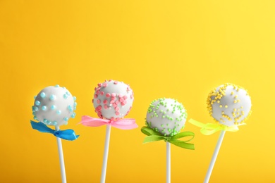 Photo of Tasty cake pops with bows on yellow background