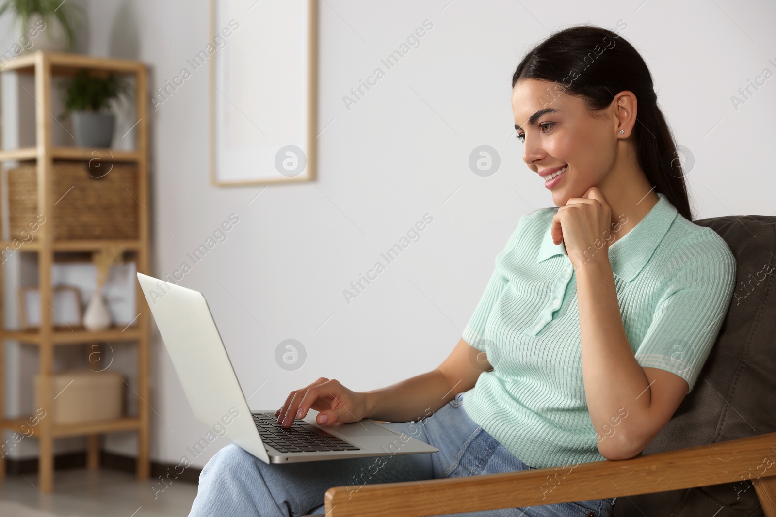 Photo of Young woman working with laptop in armchair at home