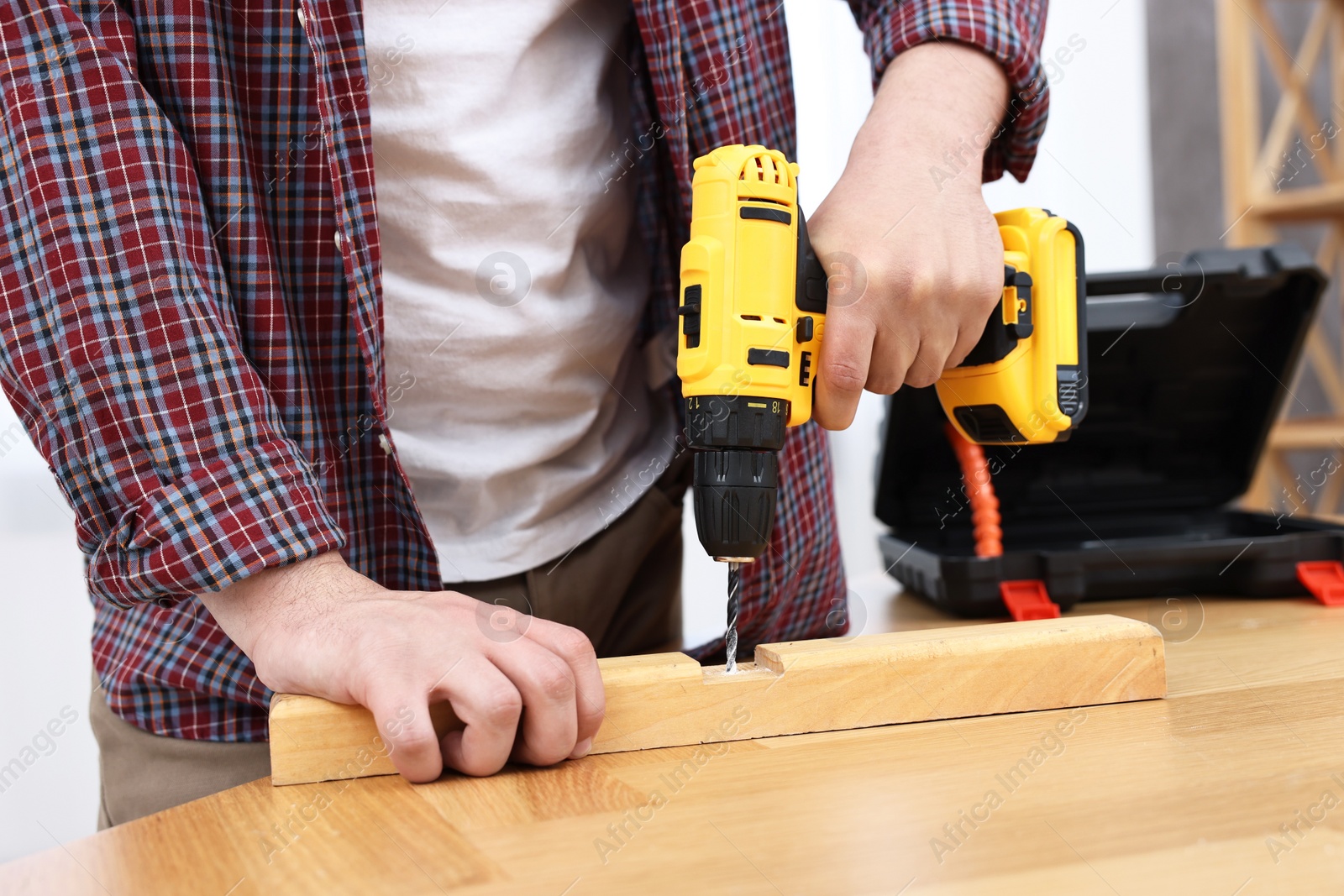 Photo of Young handyman working with electric drill at table in workshop, closeup