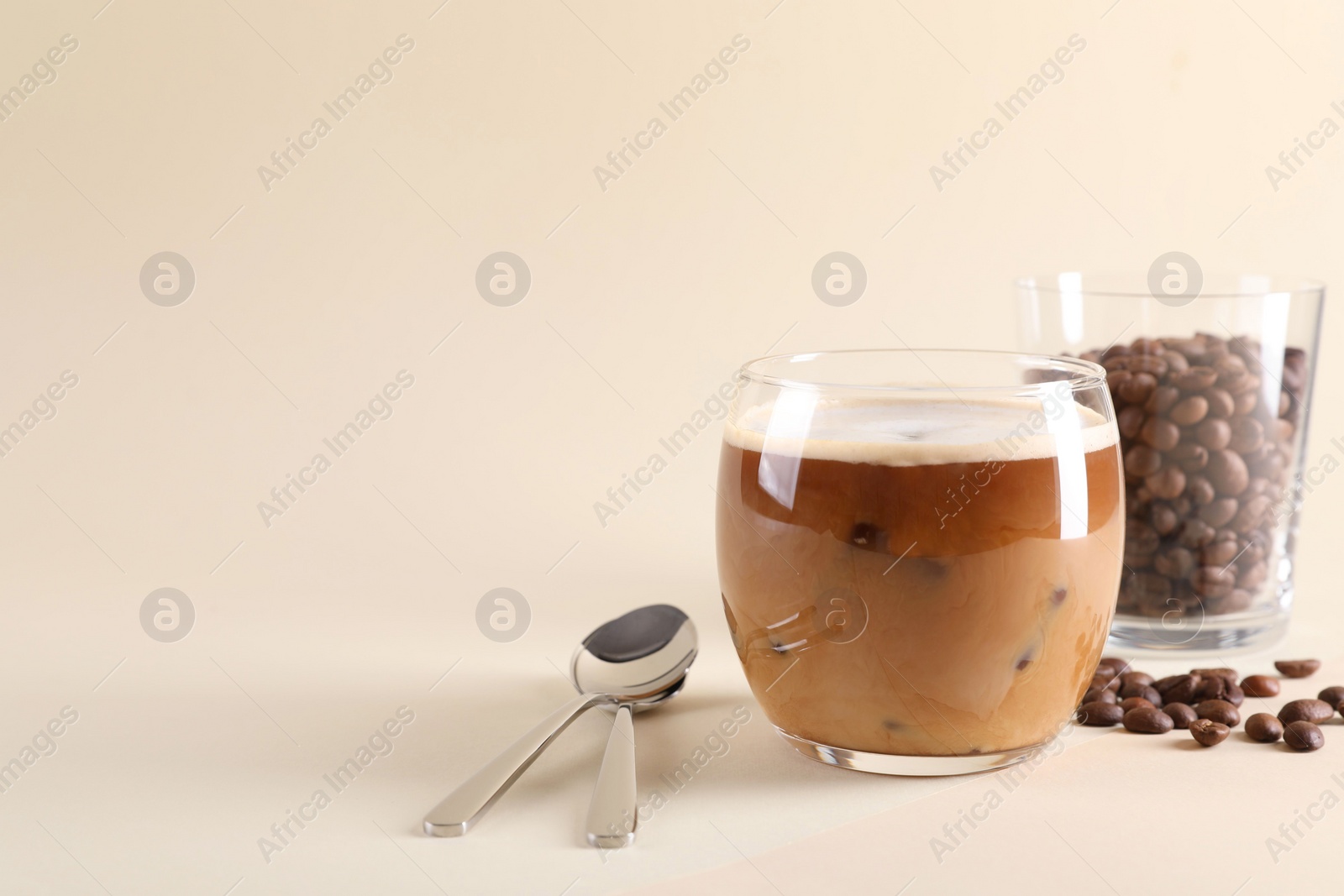 Photo of Refreshing iced coffee with milk in glass, beans and spoons on beige background, space for text