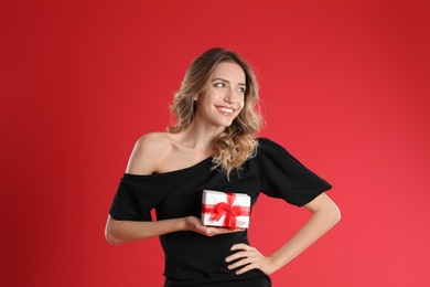 Beautiful young woman with Christmas present on red background