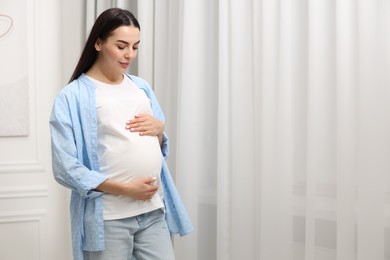 Photo of Pregnant young woman near window indoors, space for text
