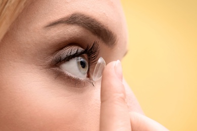 Young woman putting contact lens in her eye on color background, closeup