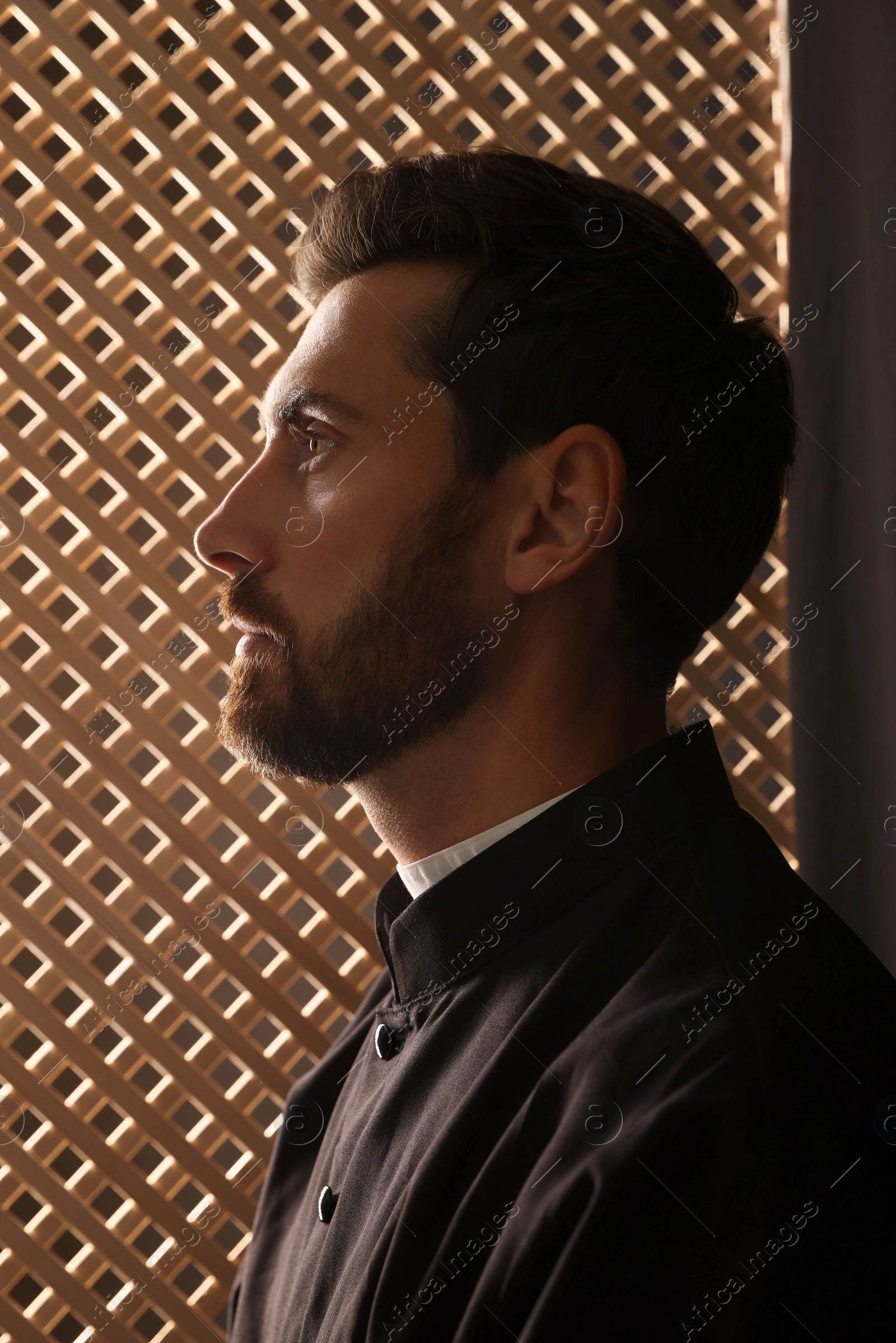 Photo of Catholic priest wearing cassock in confessional booth