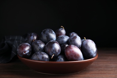 Photo of Delicious ripe plums in bowl on wooden table