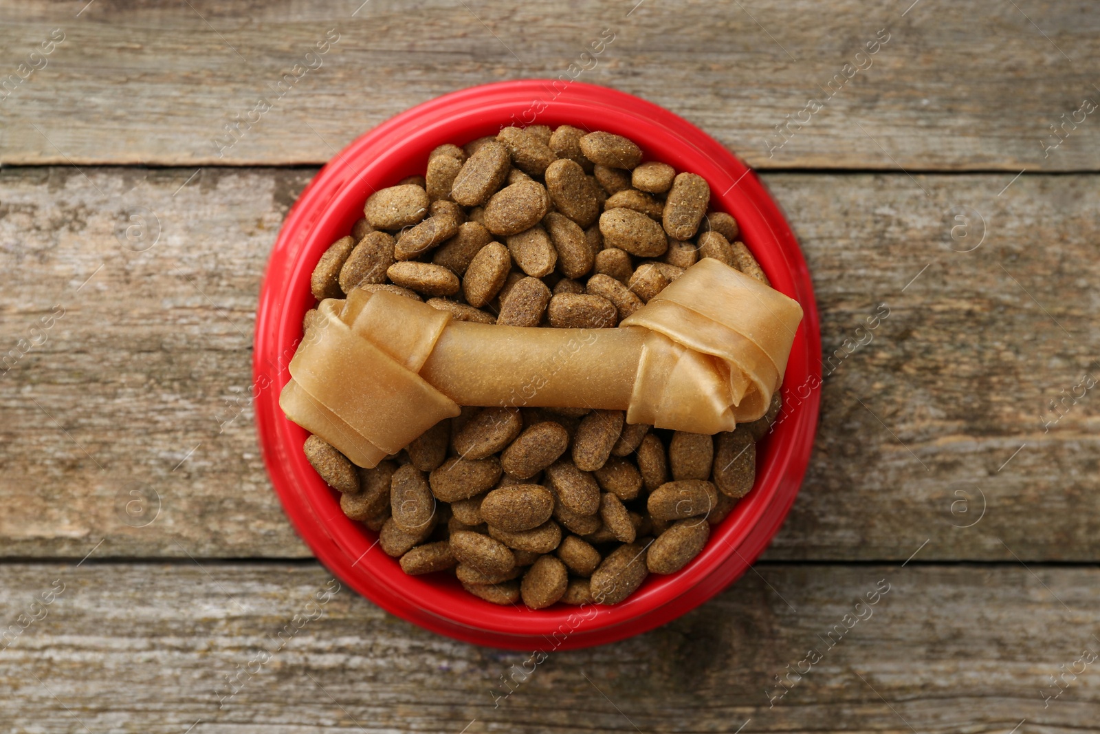 Photo of Dry dog food and treat (chew bone) on wooden floor, top view