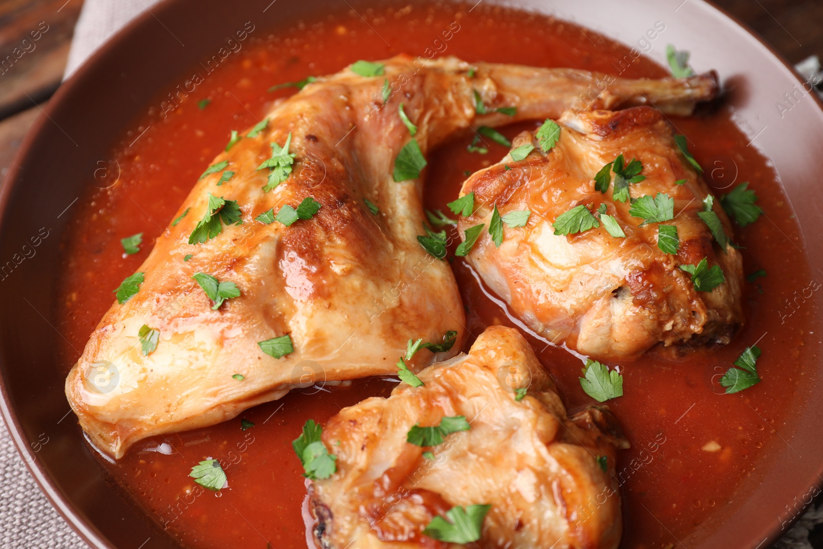 Photo of Tasty cooked rabbit meat with sauce and parsley on table, closeup