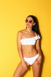 Photo of Beautiful young woman in white bikini with sunglasses on yellow background