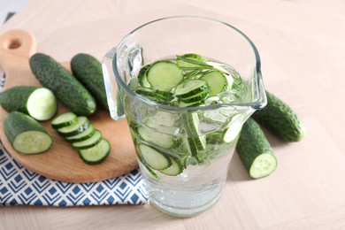 Photo of Refreshing cucumber water with rosemary in jug and vegetables on light wooden table, closeup