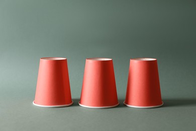 Photo of Three red cups on pale olive background. Thimblerig game
