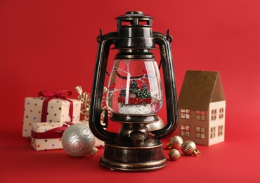 Photo of Beautiful Christmas snow globe, gift boxes and festive decor in vintage lantern on red background