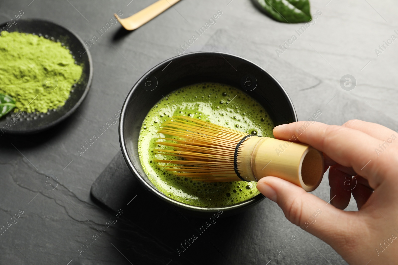 Photo of Woman preparing matcha tea at black table, above view