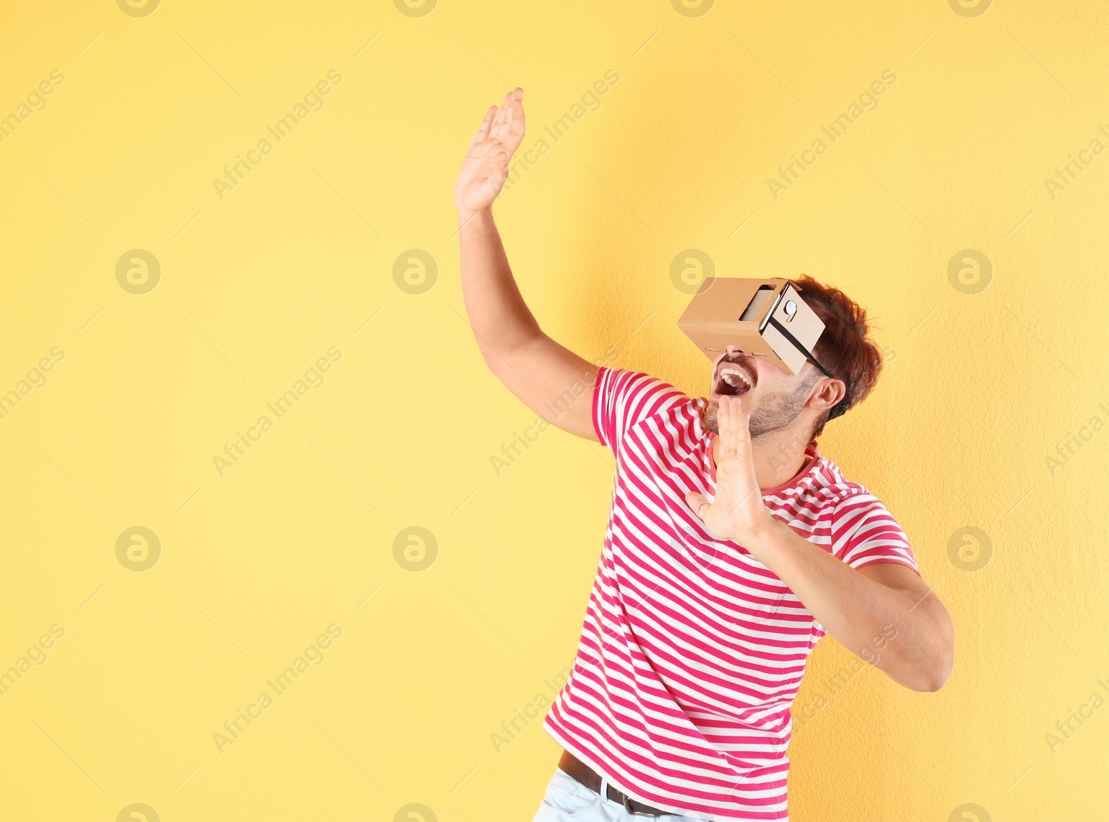 Photo of Young man using cardboard virtual reality headset on color background. Space for text