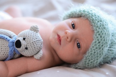 Photo of Cute newborn baby in warm hat with toy lying on bed, closeup