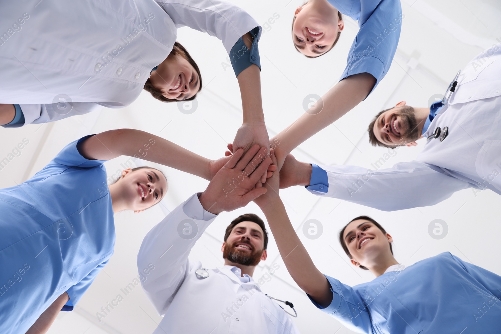 Photo of Team of medical doctors putting hands together indoors, bottom view