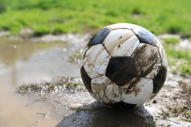 Photo of Dirty soccer ball on green grass near puddle outdoors, closeup. Space for text