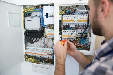 Photo of Electrician repairing fuse box with screwdriver indoors, closeup