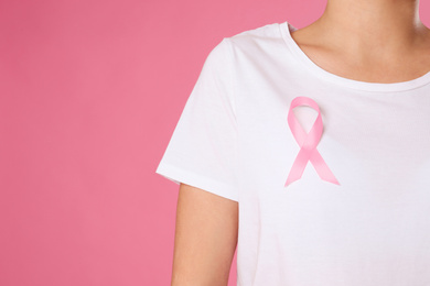 Closeup view of woman with pink ribbon on color background, space for text. Breast cancer awareness