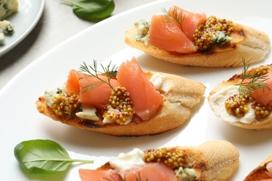 Tasty bruschettas with salmon and blue cheese on plate, closeup