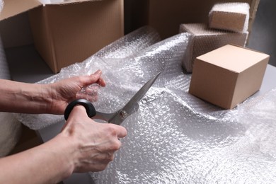 Woman cutting bubble wrap at table in warehouse, closeup